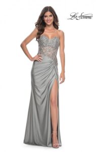 This stunning silver strapless prom dress features a ruched jersey skirt sweetheart neckline and high slit. The exquisite sheer bodice incorporates lace applique and rhinestones with open back with additional ruching along the zipper closure